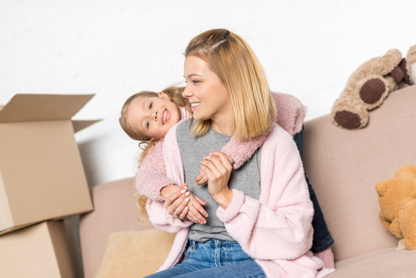 happy mother and daughter hugging while sitting on sofa during relocation - Fotografie, Obrázek