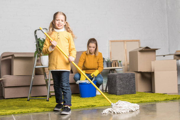 moeder en dochter schoonmaken kamer met mop en emmer terwijl het bewegen van home - Foto, afbeelding