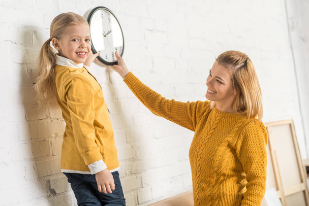 beautiful happy mother and daughter hanging clock on wall during relocation    - Fotoğraf, Görsel