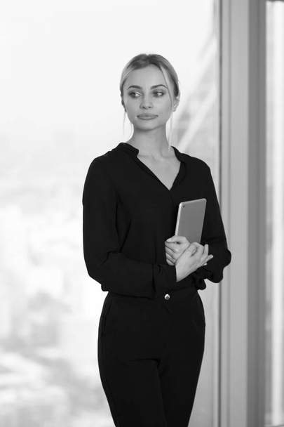 Beautiful business woman with tablet in hands stands near window in office. - Fotó, kép