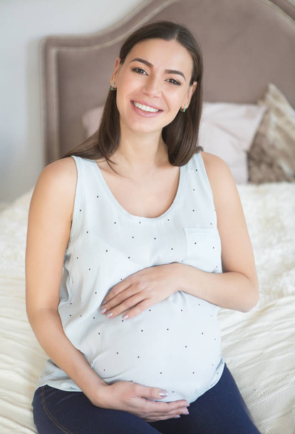 Zwangere vrouw binnenshuis zittend op het bed - Foto, afbeelding