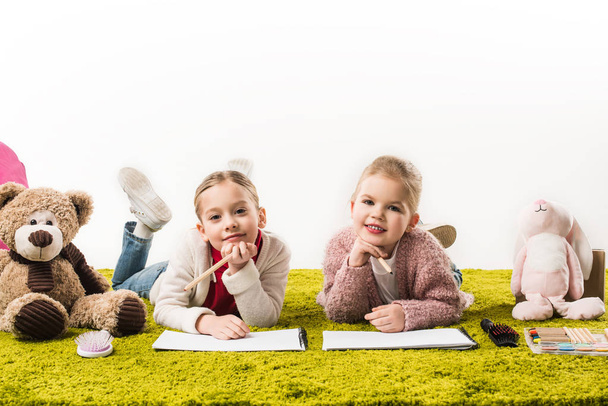 прелестные маленькие сестры рисуют цветными карандашами вместе на полу изолированы на белом
 - Фото, изображение