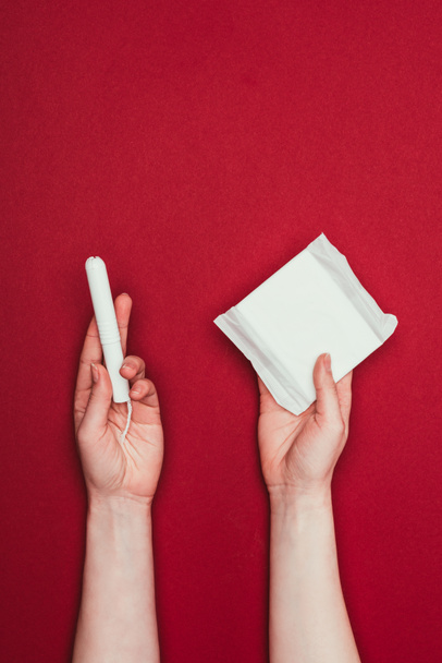 cropped shot of woman holding menstrual pad and tampon isolated on red - Fotó, kép