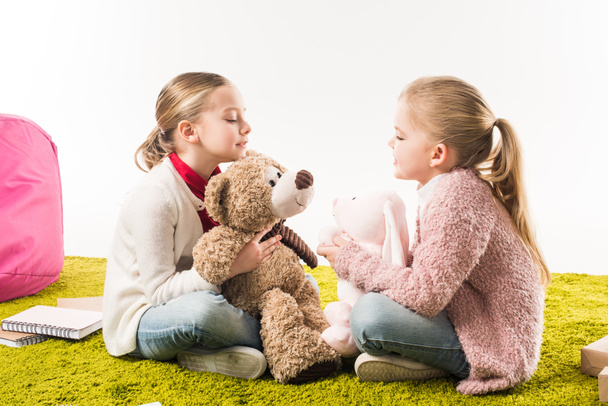 little sisters playing with soft toys while sitting on floor isolated on white - Fotografie, Obrázek
