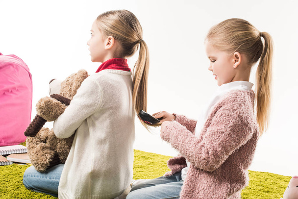 ευτυχισμένο παιδί βούρτσισμα τα μαλλιά της αδελφής του ενώ κάθεται στο πάτωμα που απομονώνονται σε λευκό - Φωτογραφία, εικόνα