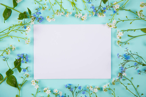 Прозорий аркуш білого паперу в оточенні синьо-білих маленьких квітів на світлому фоні м'яти
. - Фото, зображення