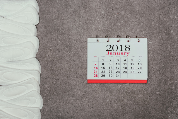 vista superior de las almohadillas menstruales dispuestas y el calendario en la superficie gris
 - Foto, imagen