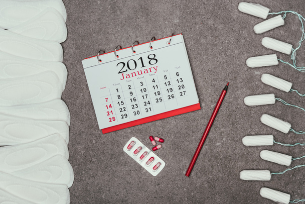 Draufsicht auf arrangierte Menstruationspads und Tampons, Kalender und Pillen auf grauer Oberfläche - Foto, Bild