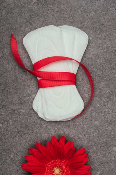top view of arranged menstrual pads with ribbon and red flower on grey surface - Photo, Image