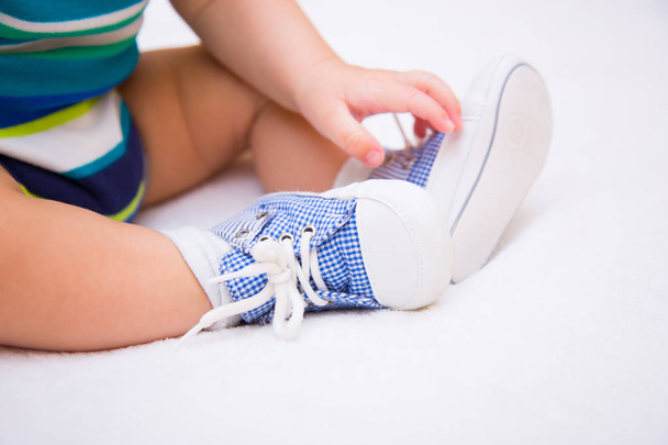Legs of baby boy dressed in children's blue sneakers on lacing on white background - Foto, imagen