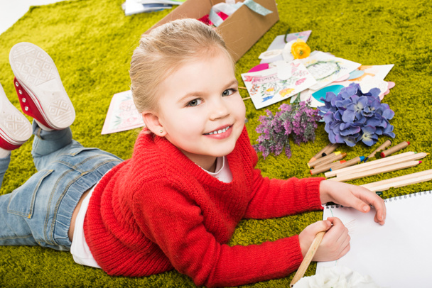 smiling  little child drawing with color pencils on green soft carpet - Photo, Image