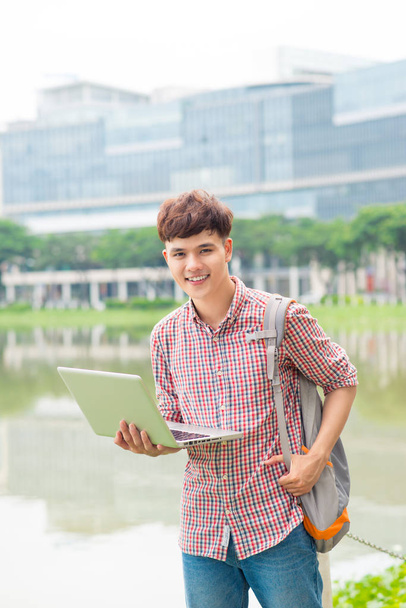 Aantrekkelijke mannelijke Aziatische student is het gebruik van laptop in campus - Foto, afbeelding