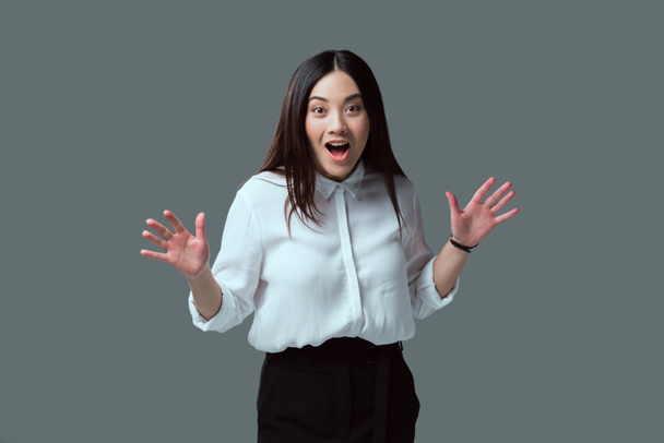shocked young woman gesturing with hands and looking at camera isolated on grey - Фото, изображение