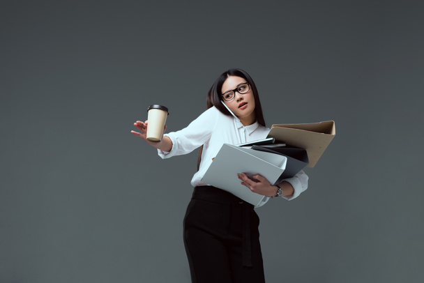 attractive businesswoman with folders and coffee to go talking by smartphone isolated on grey  - Foto, afbeelding