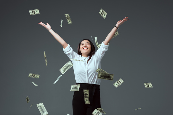 Gelukkig jonge Aziatische vrouw gooien dollar biljetten geïsoleerd op grijs - Foto, afbeelding