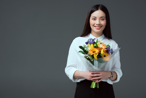 krásná asijská žena drží kytici květin a usmívá se na kameru izolované Grey - Fotografie, Obrázek