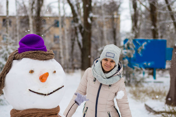 Stylish woman sculpt a big real snowman. Beautiful woman has fun in winter park, wintertime - Foto, imagen