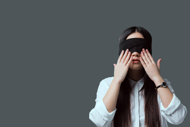 young woman in black blindfold touching face with hands isolated on grey - Foto, Imagem