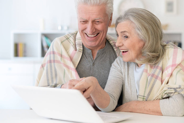 portrait of happy beautiful senior couple with blanket using laptop at home - Photo, Image