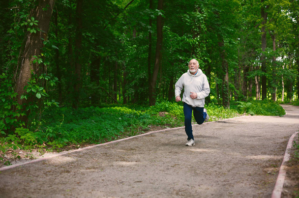 Elderly man running in green forest, copy space - Фото, изображение