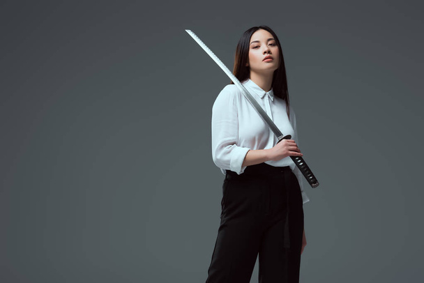 atraente jovem asiático mulher segurando katana espada e olhando para câmera isolado no cinza
   - Foto, Imagem