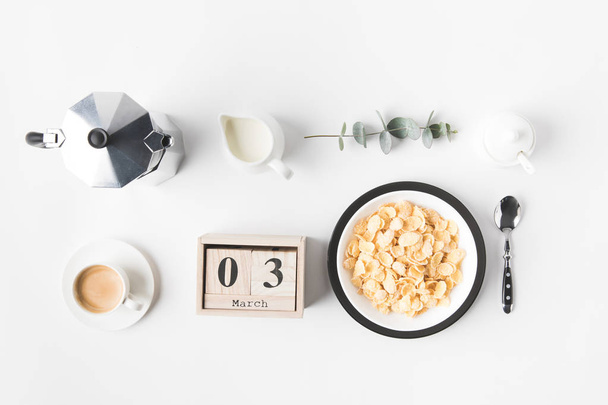 tasainen makasi maissi hiutaleet kulhoon aamiainen, kahvinkeitin ja kalenteri valkoisella pinnalla
 - Valokuva, kuva