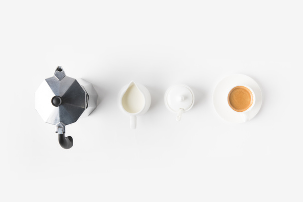 top view of arranged cup of coffee, jag of milk and coffee maker on white surface - Fotoğraf, Görsel