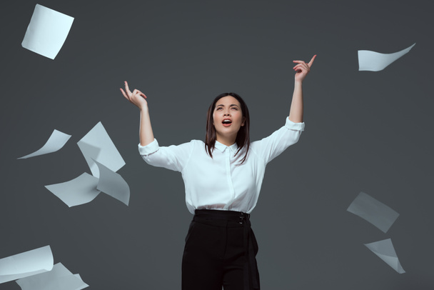 emotional young businesswoman throwing papers isolated on grey - Foto, imagen