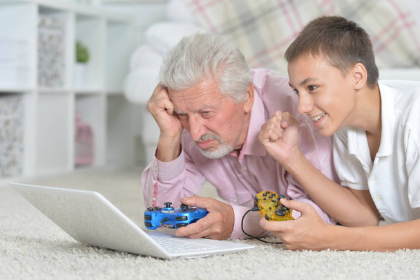 grand-père et petit-fils couchés sur le sol et jouant à des jeux informatiques sur ordinateur portable
 - Photo, image