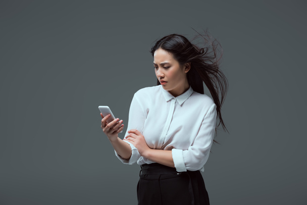 serious young asian woman using smartphone isolated on grey - Fotografie, Obrázek