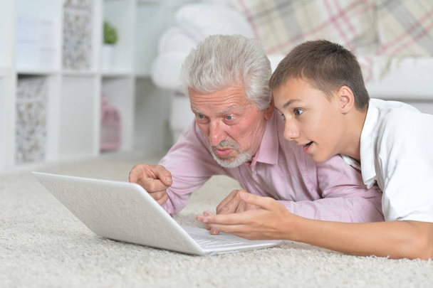 grandfather and grandson lying on floor and using laptop - Photo, Image