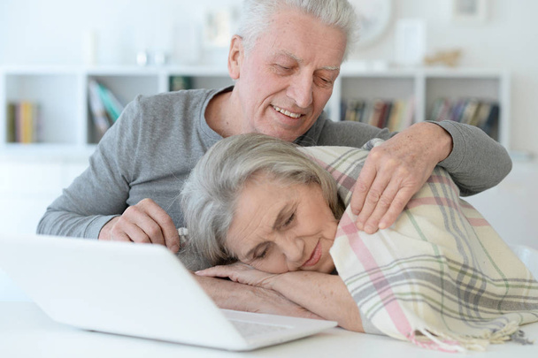 portrait of senior man hugging beautiful senior woman with blanket who sleeping near laptop at home - Foto, imagen