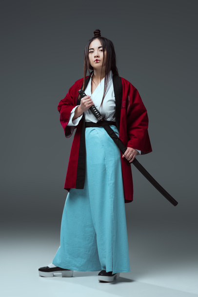 samurai in kimono holding katana sword and looking at camera on grey - Photo, Image