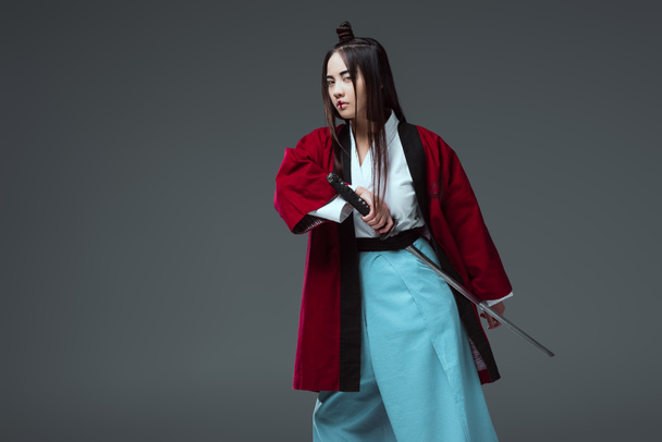 Aziatische vrouw in kimono katana zwaard houden en kijken naar camera geïsoleerd op grijs  - Foto, afbeelding
