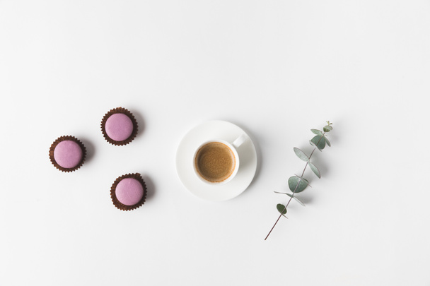 Draufsicht auf arrangierte Tasse Kaffee, Desserts und Pflanze auf weißer Tischplatte - Foto, Bild