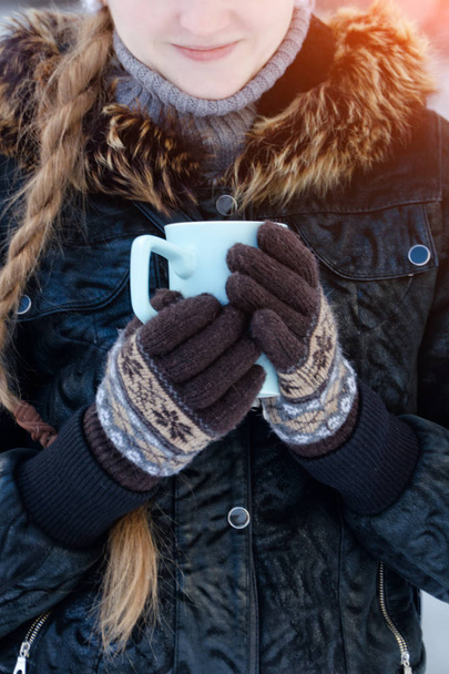 Mädchen in den braunen Handschuhen hält einen blauen Becher Tee, ein Teil des Gesichts - Foto, Bild