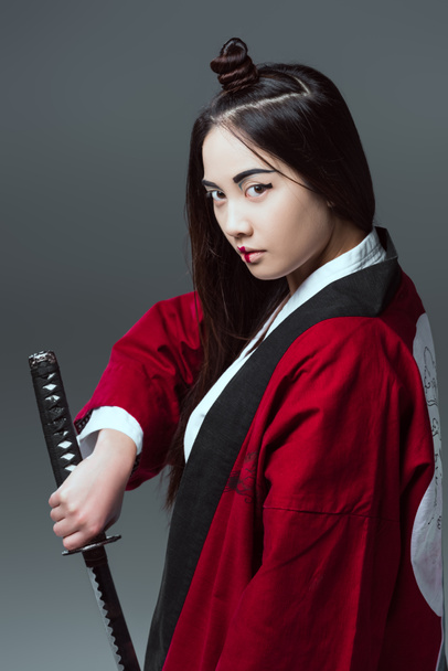 young asian woman in kimono holding katana and looking at camera isolated on grey - Photo, Image