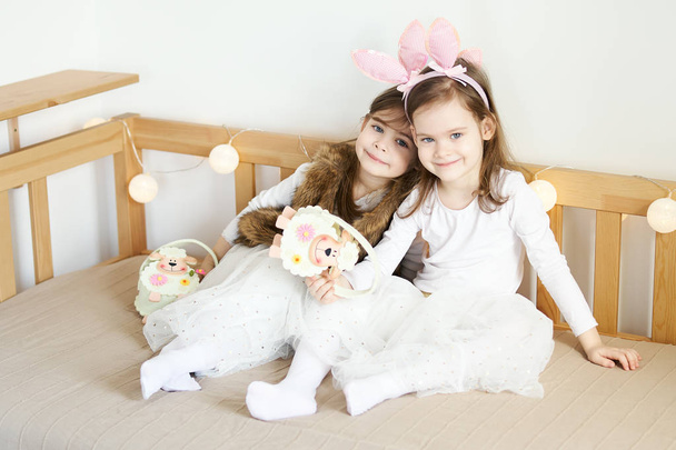 Девочки в кроличьих ушах сидят на диване с пасхальными корзинами
 - Фото, изображение