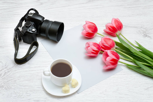 Photo camera, mug of coffee and pink tullips. Wooden  background - Photo, Image