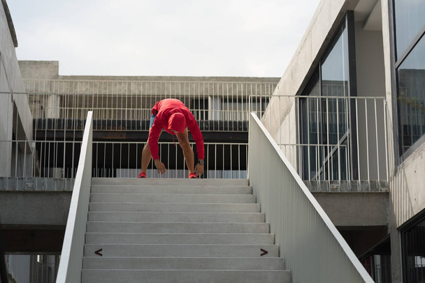 Sport man in red hood doing exercise on steps outdoor. - Foto, immagini