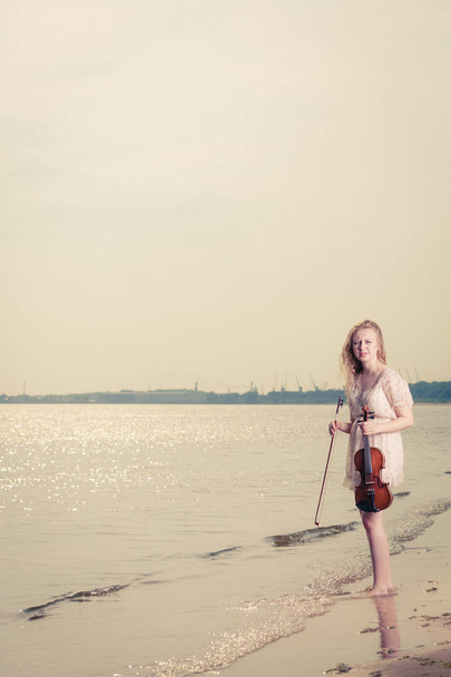 Woman on beach near sea holding violin - Photo, image