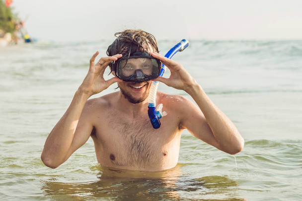 Mies, jolla on naamio ja snorkkeli, sukeltaa mereen.
. - Valokuva, kuva