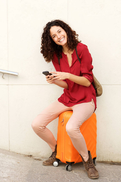 Portrait of travel woman sitting on suitcase and using smartphone - Zdjęcie, obraz