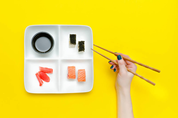 Female hand with chopsticks and plate with sushi - 写真・画像