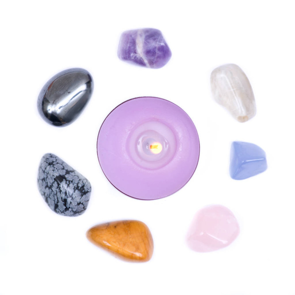 Lavendel thee licht kaars omringd door set van zeven helende chakra stenen voor kristalhealing, geïsoleerd op witte achtergrond  - Foto, afbeelding
