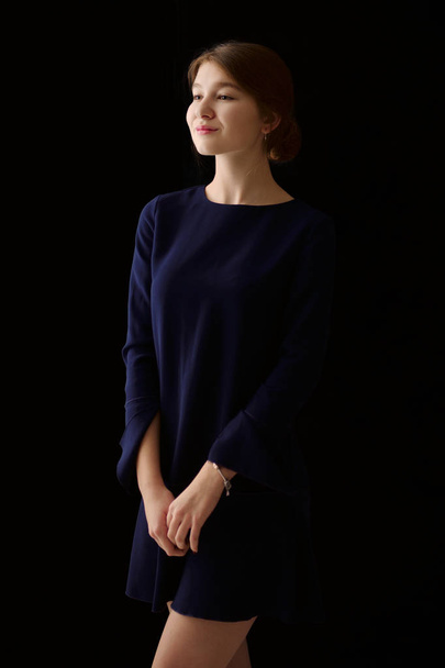 Low key portrait of pretty girl in short dress posing on dark background. Blank for a layout. - Zdjęcie, obraz