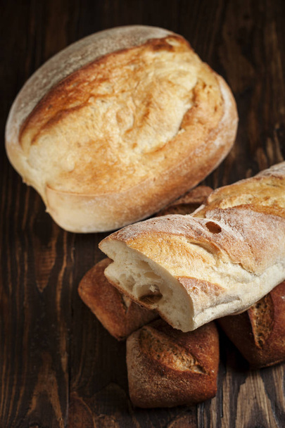 frisch gebackenes Brot auf einem Holztisch vor dunklem Hintergrund - Foto, Bild