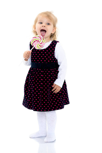 A little girl licks a candy on a stick. - Photo, Image