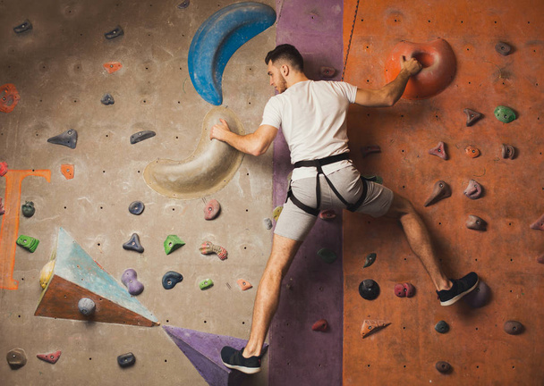 Fiatal férfi mászás mesterséges szikla fal tornaterem - Fotó, kép