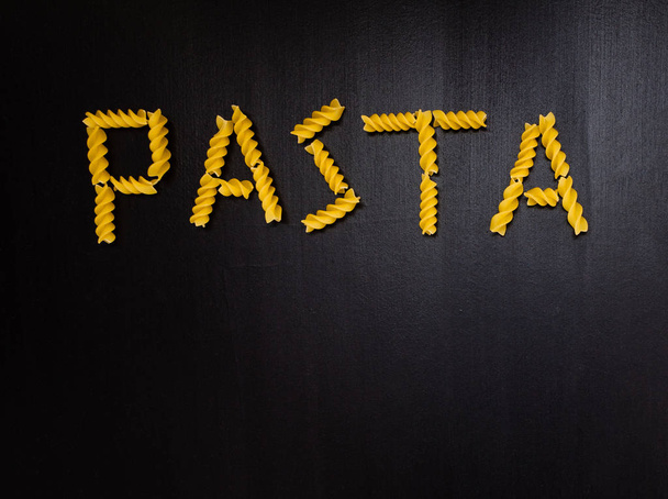 Word pasta made of yellow dry pasta on the black background. Five letters made from pasta - Foto, Bild